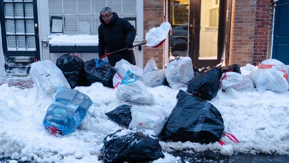 Key Lim, 55, of Quincy, removes snow from a sidewalk lined with trash bags in front of the laundromat that he manages on Tuesday, Feb. 24, 2026, in Boston. (AP Photo/Sophie Park)