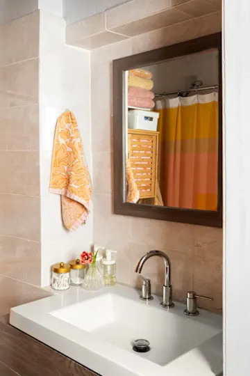 Bathroom corner featuring a white sink, chrome faucet, decorative towels, and a mirror reflecting colorful shower curtains.