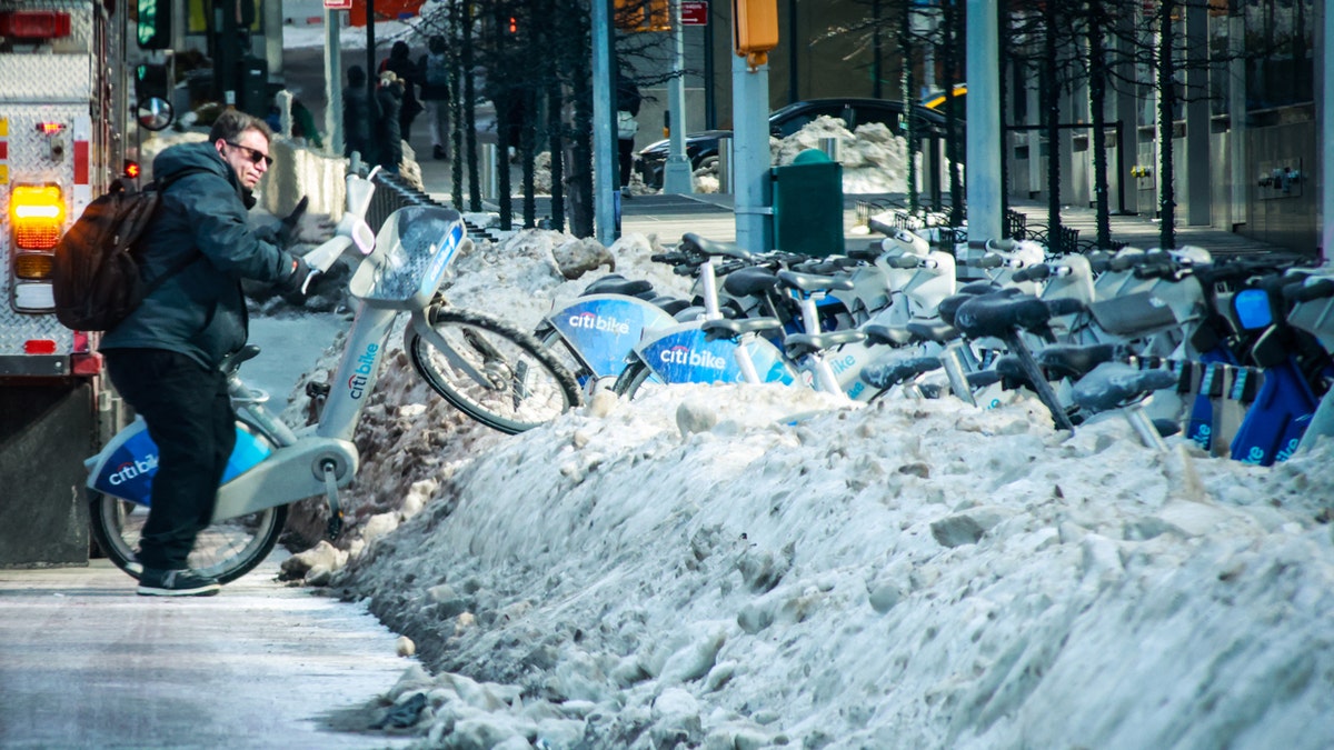 A man removing a bicycle from a bikeshare station during a snowstorm in Midtown Manhattan.