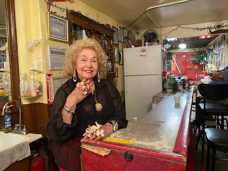 Maria Antonia Cay, better known as Toñita, shows off her bedazzled rings behind the bar where she serves beer to her clients.