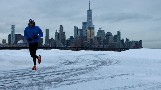 HOBOKEN, NJ - JANUARY 26: A person jogs along a snow-covered walkway in front of the skyline of lower Manhattan and One World Trade Center in New York City on January 26, 2026, in Hoboken, New Jersey.