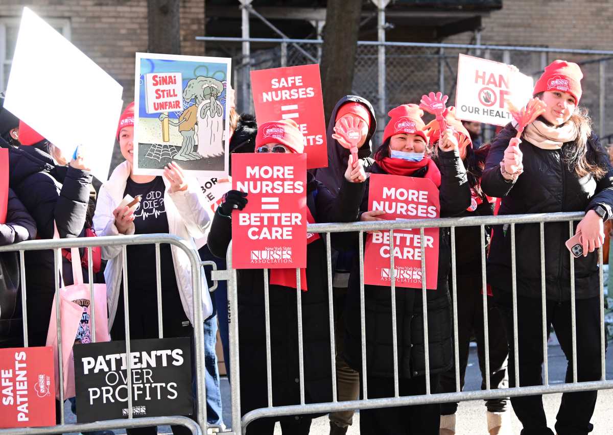 group of people wearing red behind metal barrier during nurses strike