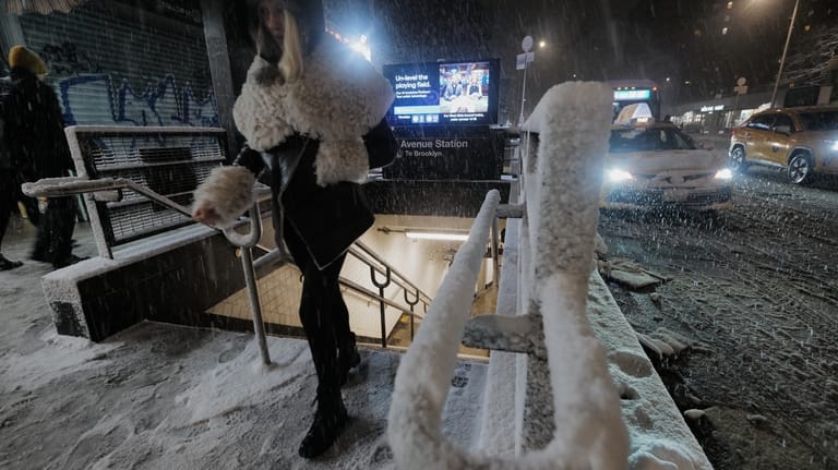 A passenger exits a subway station as snow falls in...