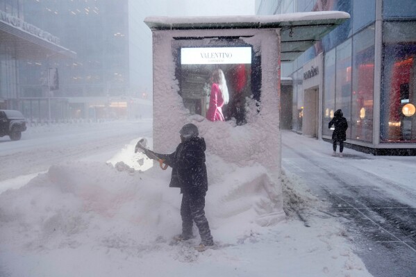 A man shovels snow around a news stand during a snow storm, Monday, Feb. 23, 2026, in New York. (AP Photo/Seth Wenig)