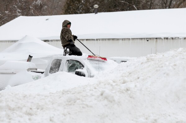 A man clears snow off of cars and trucks in a contractor's parking lot, Monday, Feb. 23, 2026, in St. James, N.Y. (AP Photo/Heather Khalifa)