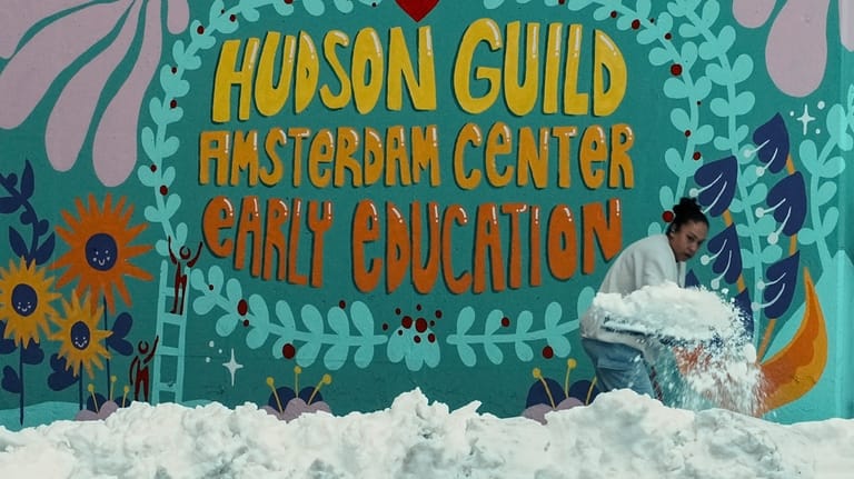 A woman clears snow from a walk outside a preschool,...