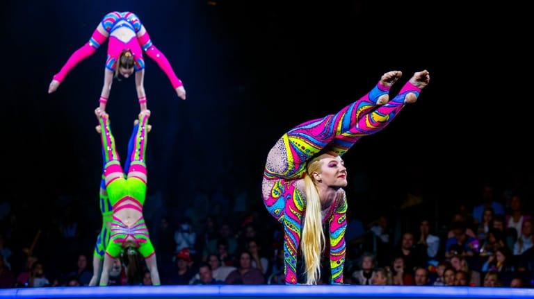 Acrobats contort in colorful garb to a pop music soundtrack...