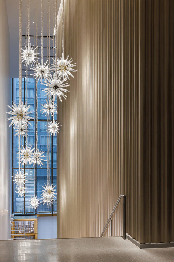 Modern interior with tall, golden vertical panels and a row of contemporary starburst chandeliers beside large windows.