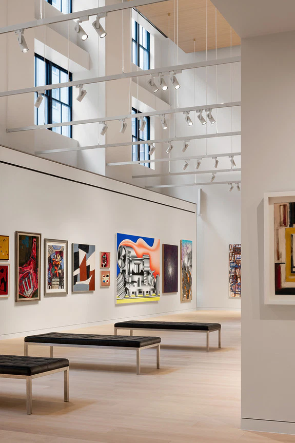 Modern art gallery interior with contemporary paintings on white walls and wooden benches.