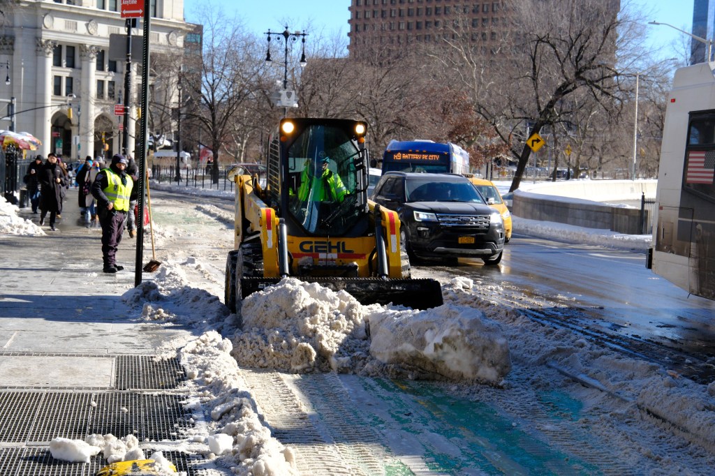 A snow removal crew clears snow from a New York City street with a front loader.