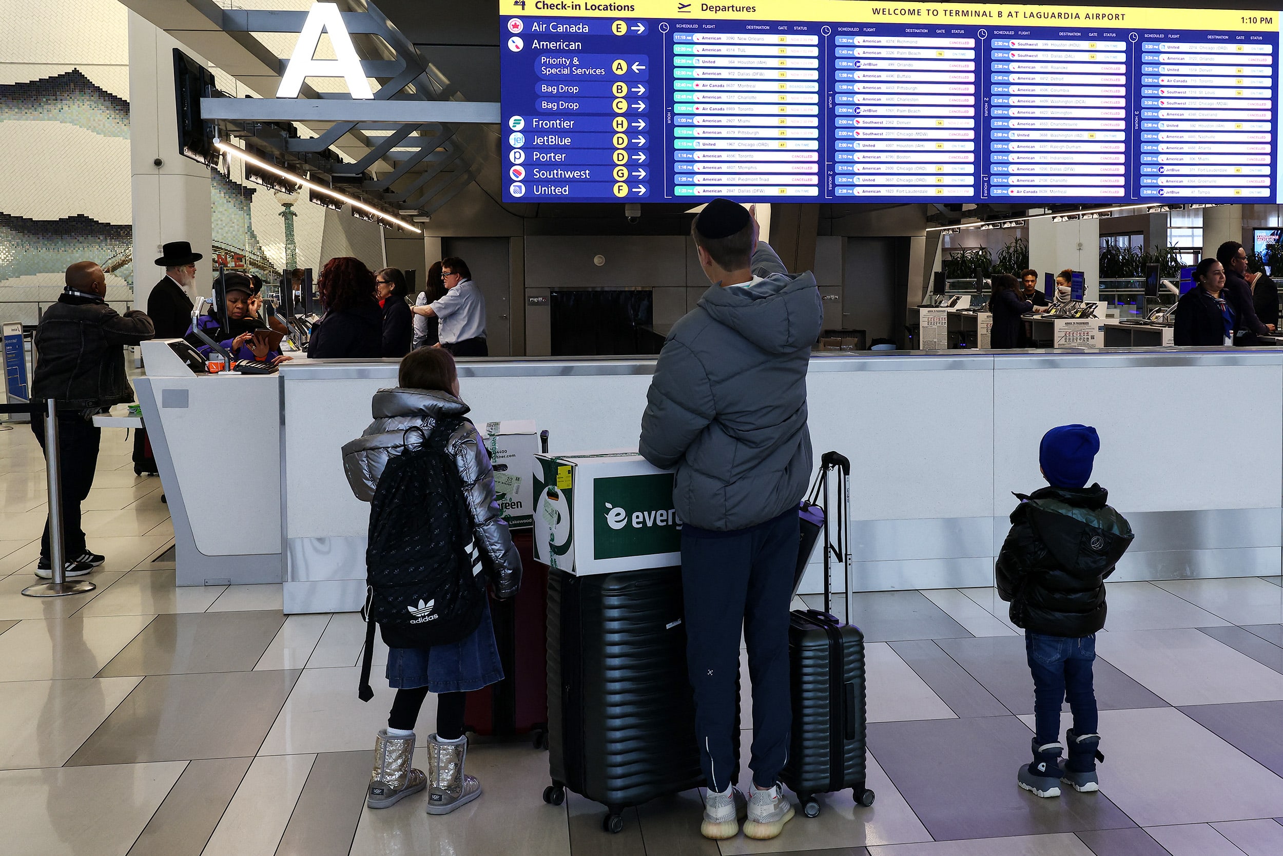 Travelers look at a flight information display board showing several flights cancelled due to weather at LaGuardia Airport in New York on February 22, 2026.