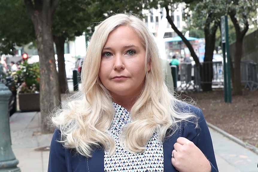 woman with white blonde hair and wearing a navy suit looks down the camera