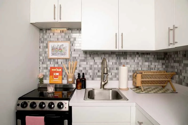 Modern kitchen corner with a stainless steel sink, stove, decorative backsplash, and wooden dish rack.