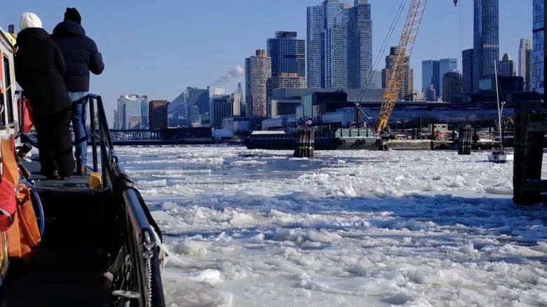 Two people standing on a Coast Guard cutter as it works to break ice in New York City