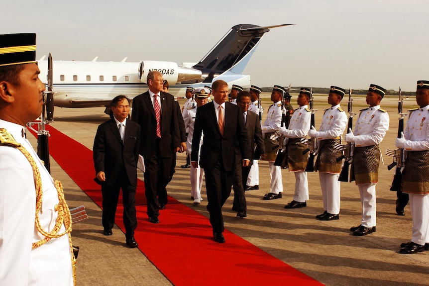 A man walks down a red carpet leading from a plane