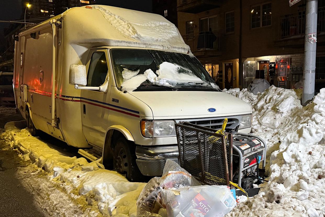 A snow-covered mobile vet clinic is parked on a snowy street in Queens, with a generator visible in front.