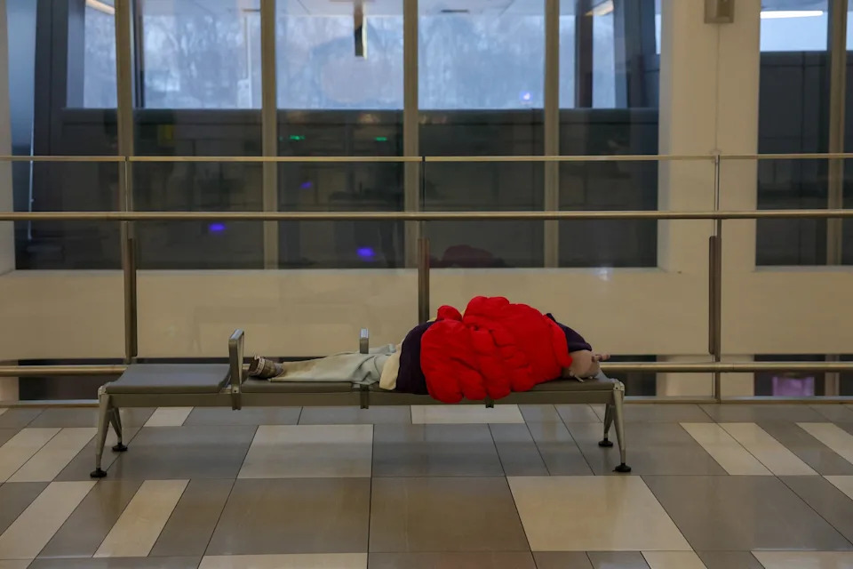 Shannon Stapleton/Reuters - PHOTO: A person sleeps on a bench during a winter storm at LaGuardia Airport in New York, Feb. 23, 2026.