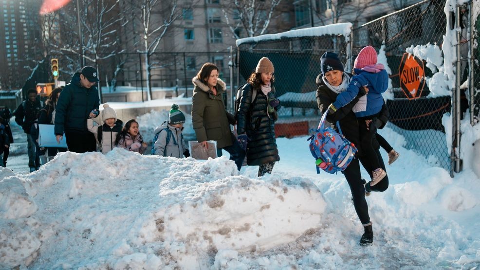 A woman carries a child over piles of plowed snow as she walks a girl to school, Tuesday, Feb. 24, 2026, in New York. (AP Photo/Eduardo Munoz Alvarez)