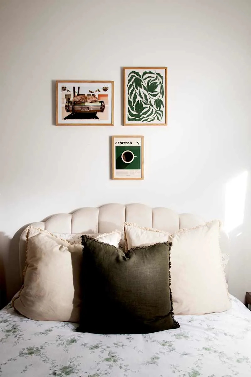 Cozy bed with a tufted headboard, decorative pillows, and framed art on the wall above.