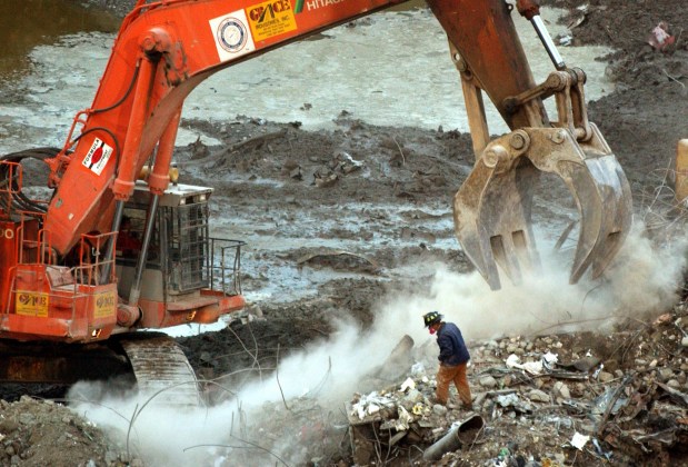 In this Jan. 8, 2001 file photo, a rescue worker wearing a dust mask, peers through a cloud of dust created by an excavator at the World Trade Center site in New York. (AP Photo/Mark Lennihan, File)