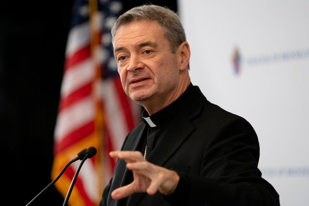 Vatican Brooklyn Bishop Robert Brennan speaking at a podium with an American flag behind him.