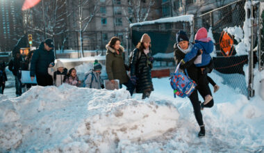 A woman carries a child over piles of plowed snow as she walks a girl to school, Tuesday, Feb. 24, 2026, in New York. Photo: Eduardo Munoz Alvarez/AP