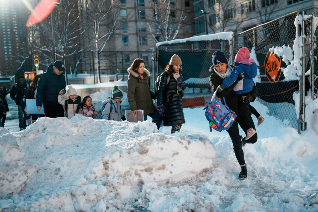 A woman carries a child over piles of plowed snow as she walks a girl to school, Tuesday, Feb. 24, 2026, in New York. Photo: Eduardo Munoz Alvarez/AP