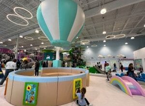 Large indoor playroom with climbing structures, floor games, and a play hot air balloon