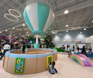 Large indoor playroom with climbing structures, floor games, and a play hot air balloon