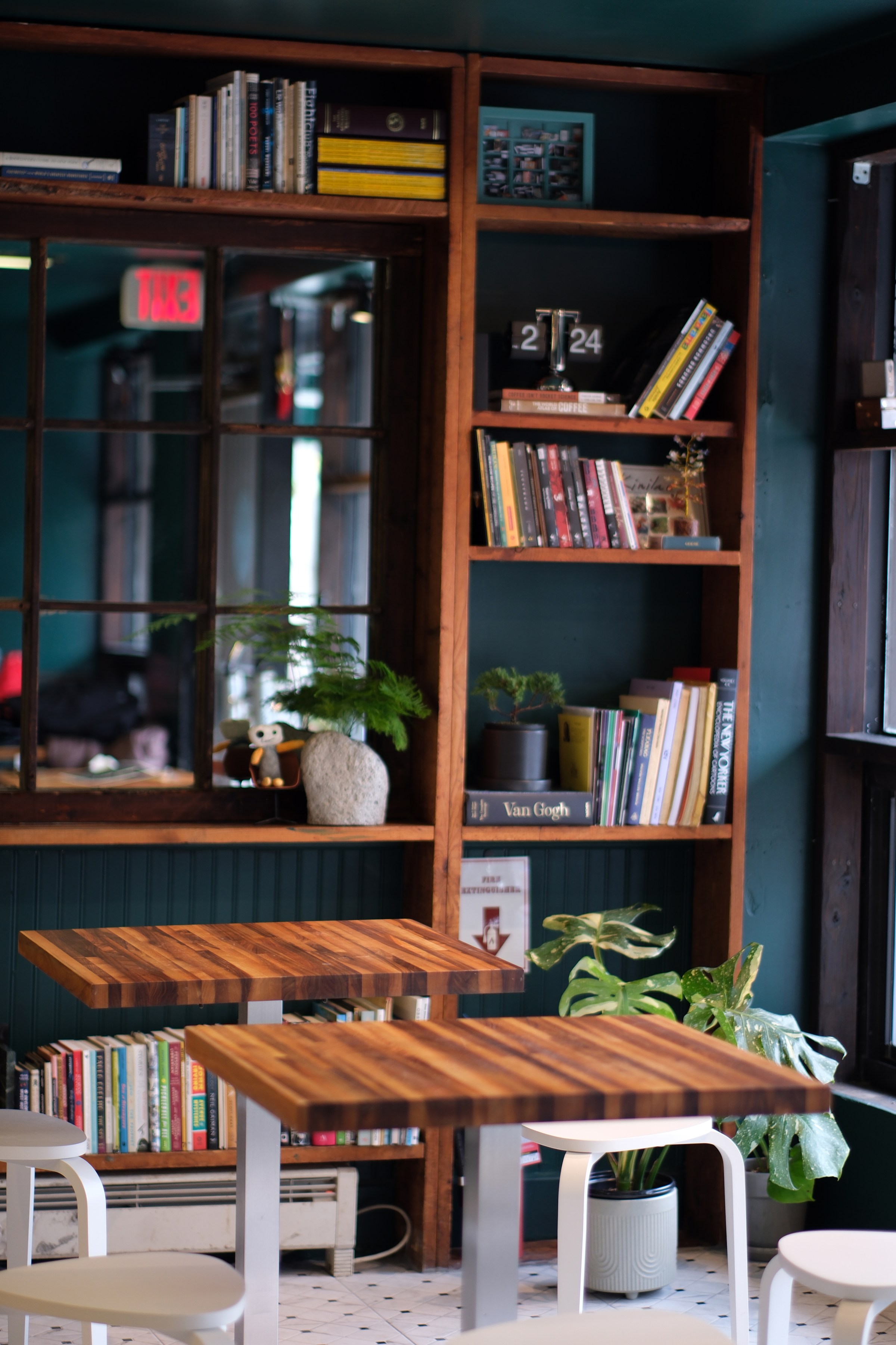 A cafe dining room with book shelves in the back and wooden tables and white chairs.