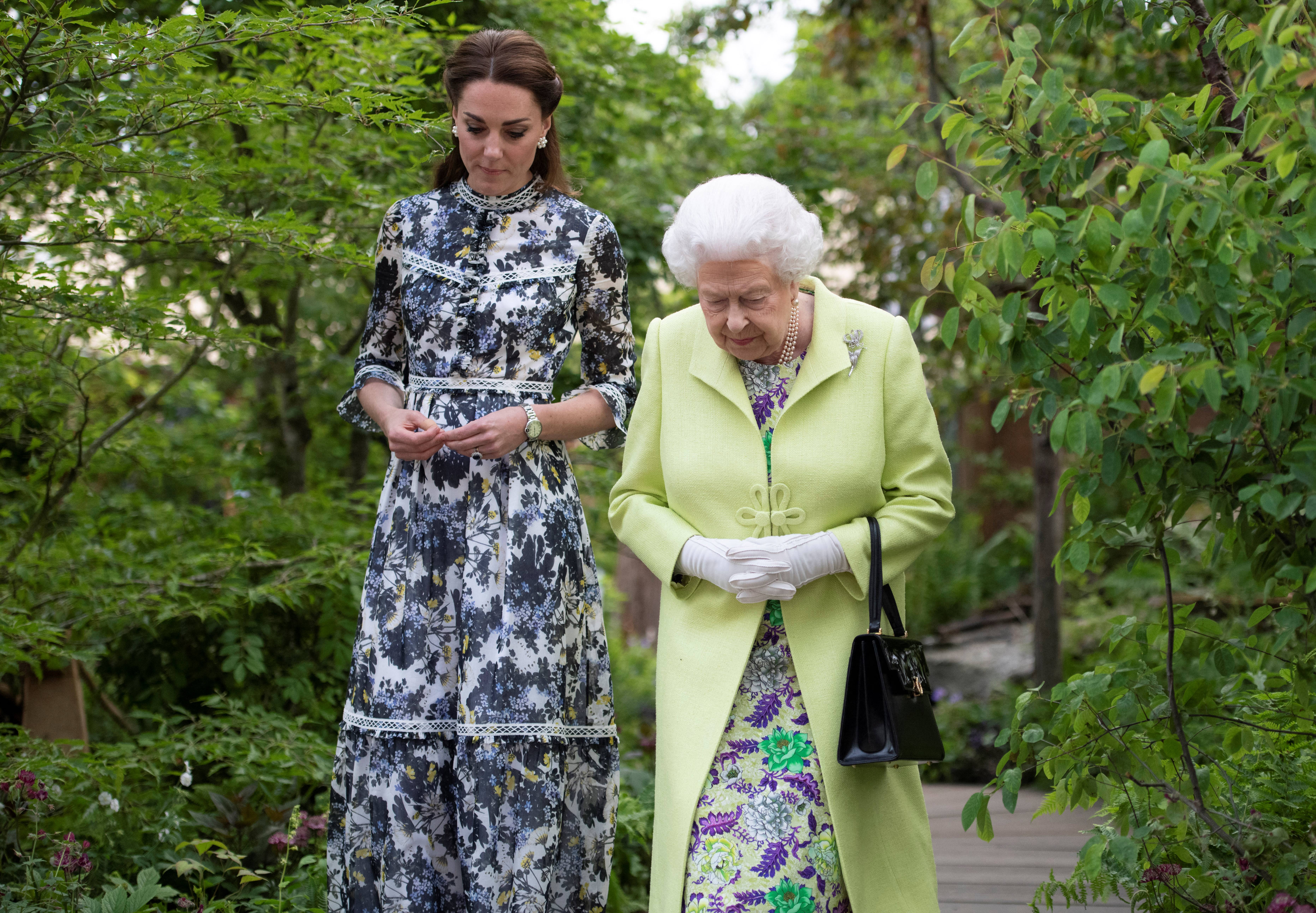 Queen Elizabeth walking next to Kate Middleton in a garden, both in floral dresses