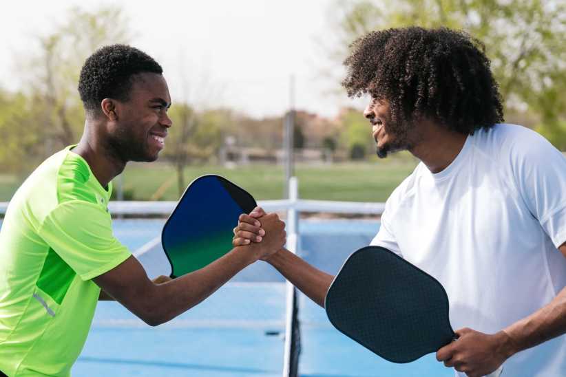 Two African players smile and shake hands over the net on the pickleball court. Concept of sportsmanship, African ethnicity, and camaraderie.