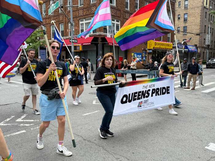 The lead banner proceeds along the parade route at Queens Pride 2025.