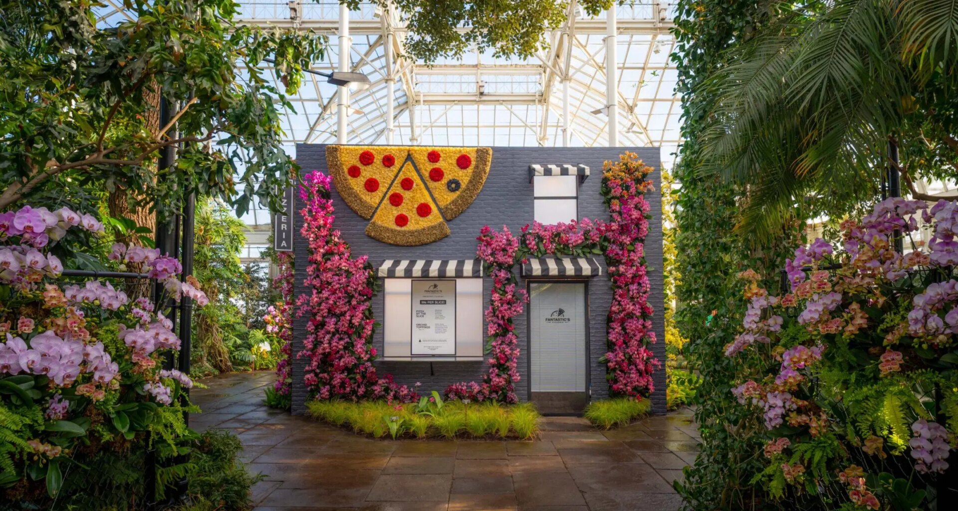 Botanical garden with a small brick building adorned with floral displays and a large pizza slice decor.