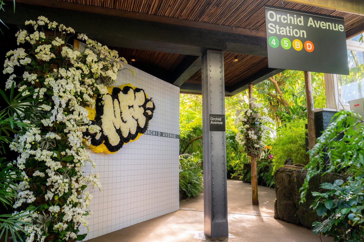 Entrance to Orchid Avenue Station with floral decorations and graffiti art under a wooden canopy.