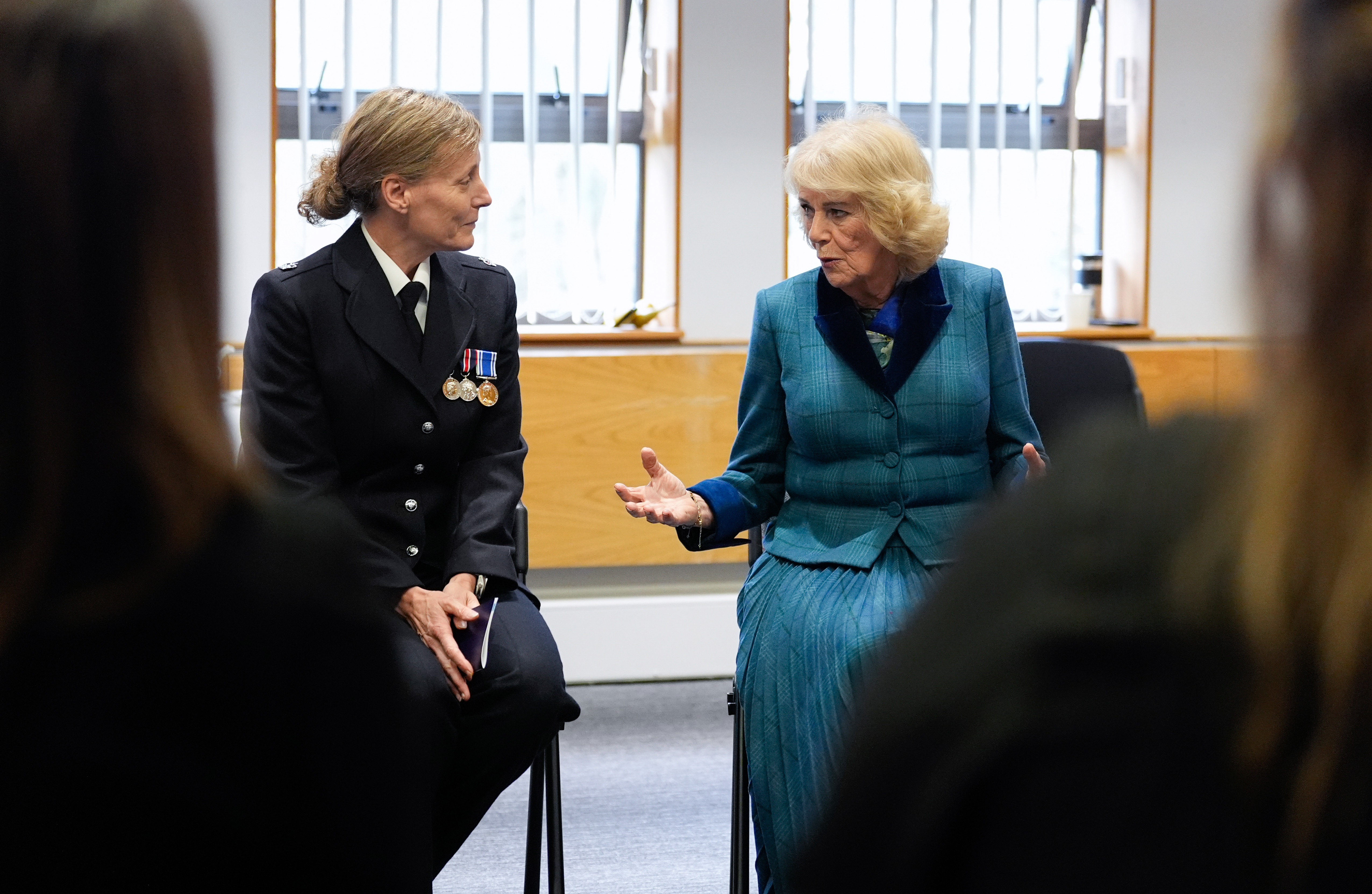 Queen Camilla sitting in a chair speaking to a police officer