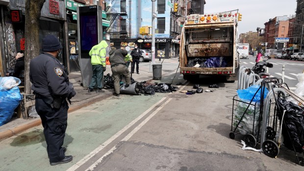 An NYPD officer, part of a team of sanitation, homeless outreach and police officers, watches as Department of Sanitation workers clean-up trash bags left by a homeless person at 9th St. and First Ave. in Manhattan on March 30, 2022. (Luiz C. Ribeiro for New York Daily News)
