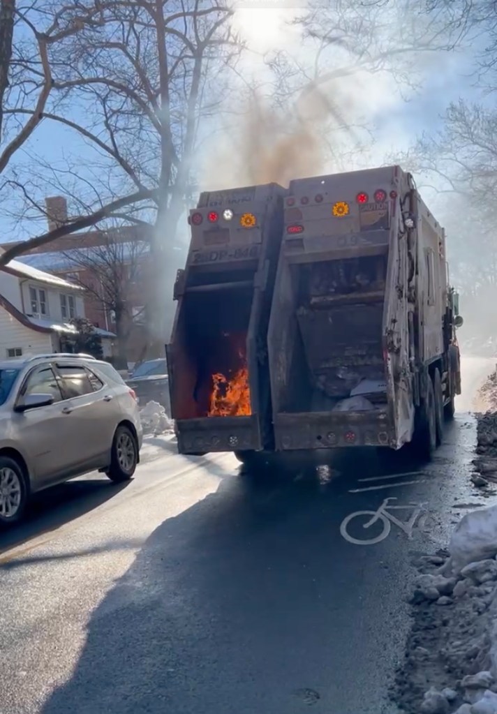 A garbage truck with a fire inside its compactor, emitting smoke.