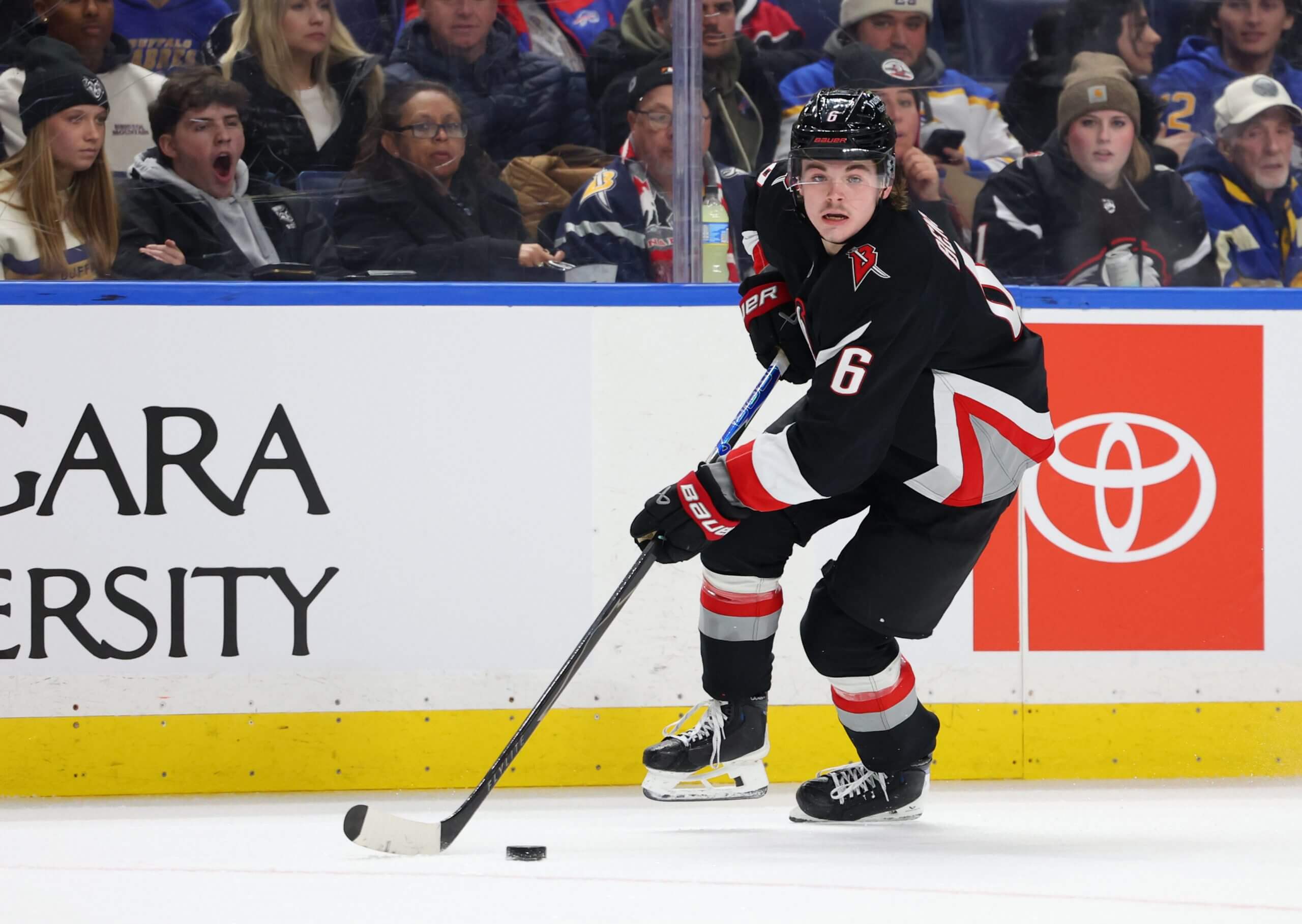 Zach Benson skates with the puck near the boards during a Sabres game.