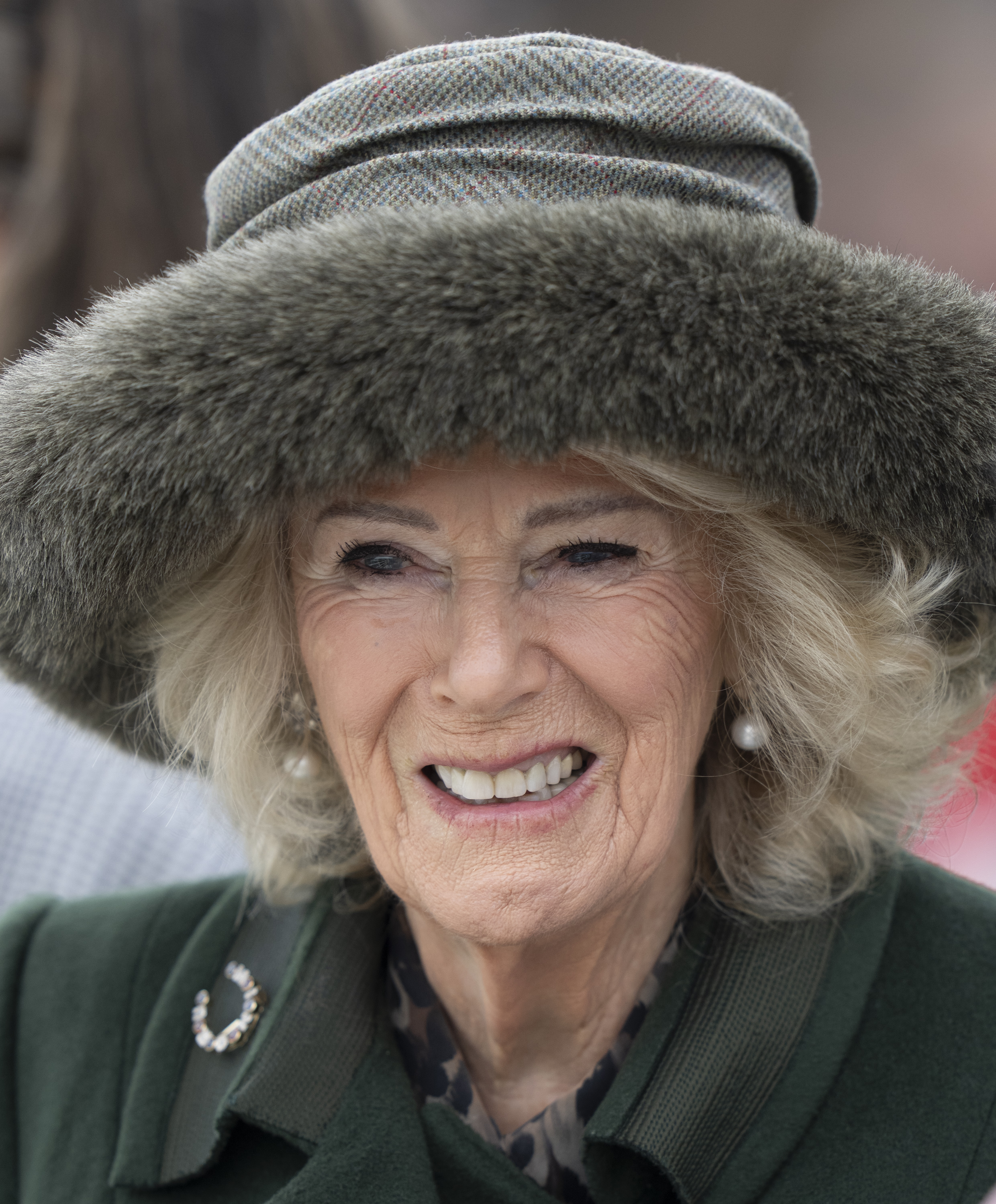 Queen Camilla wearing a green coat and fur hat and laughing