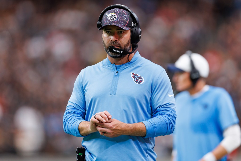 Tennessee Titans coach wearing a headset and light blue team jacket with his hands clasped.