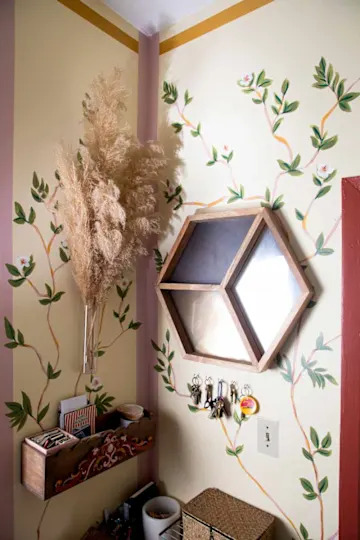Decorative entryway with floral wall art, a hexagonal mirror, a key holder, and a wooden shelf with art supplies.