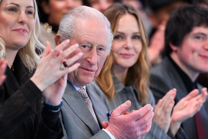 A man in a suit claps on the sidelines of a fashion show.