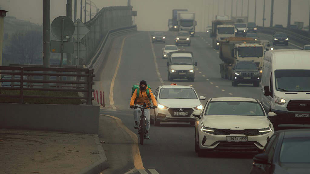 Motorcyclist riding on busy city street with heavy traffic and smog, environmental impact of urban pollution.