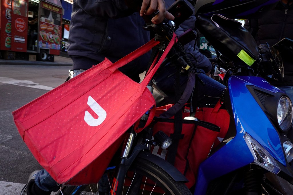 A red DoorDash delivery bag hangs from handlebars of a scooter.