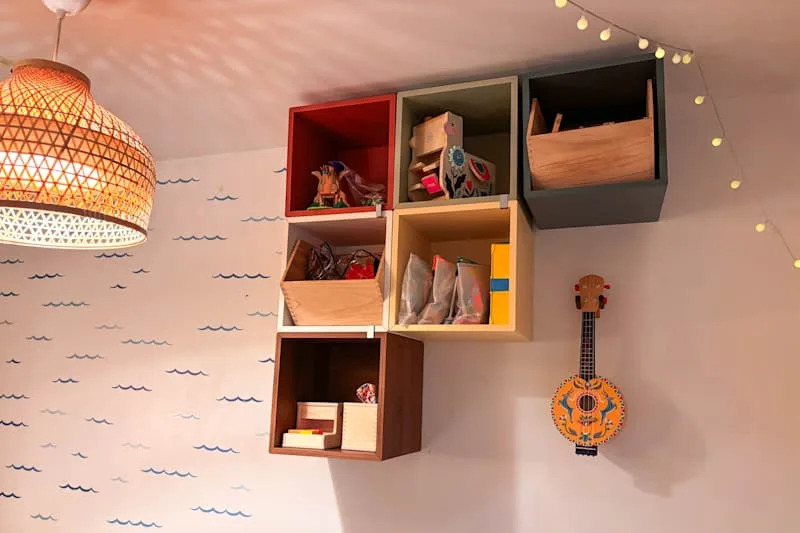 Colorful wall-mounted storage boxes filled with toys, a decorative ukulele, and a woven pendant light.