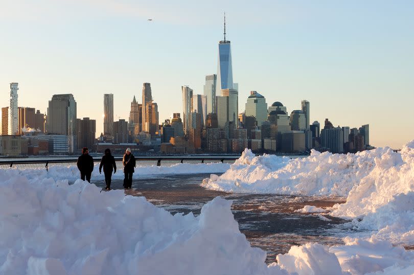People walk in front of the skyline of lower Manhattan