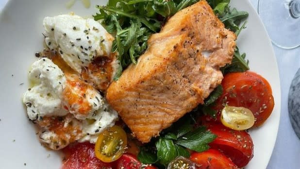 A plate of salmon on a bed of spinach, surrounded by tomatoes and cheese