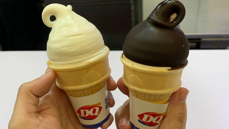 Hands holding up DQ vanilla- and chocolate-dipped soft serves in cones