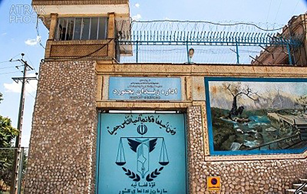 The entrance to Bojnourd Prison in Iran, featuring a gate with the scales of justice emblem and a guard tower above.